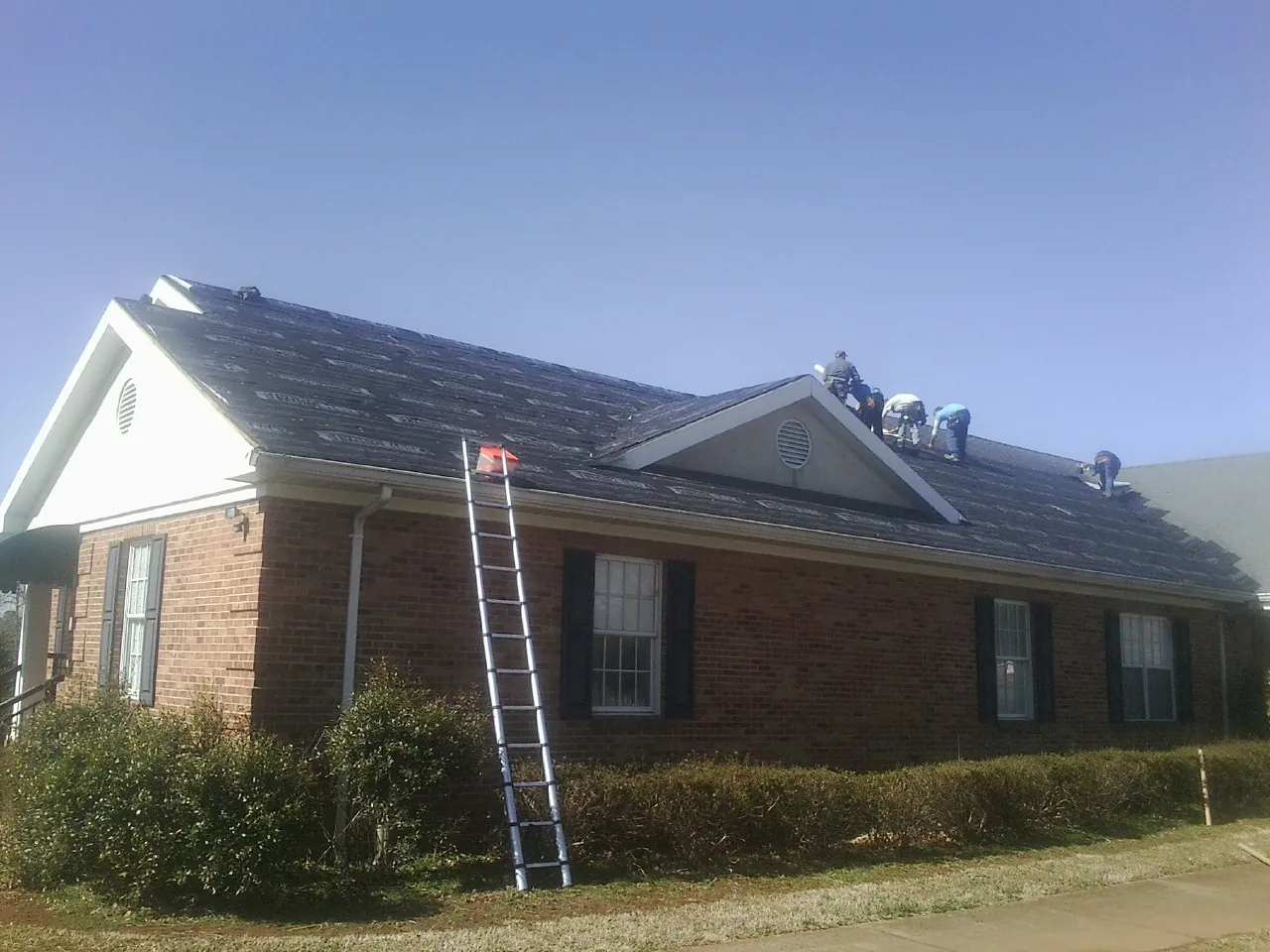 Crew tearing shingles off a brick ranch roof with a ladder set — Metal Roof Repair work by our crew in Amenia