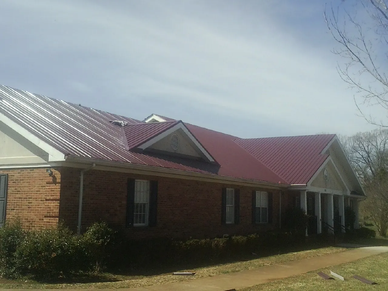 Red metal roof with gabled entries on a long brick building, from a Hail Damage Roof Repair job in Amenia