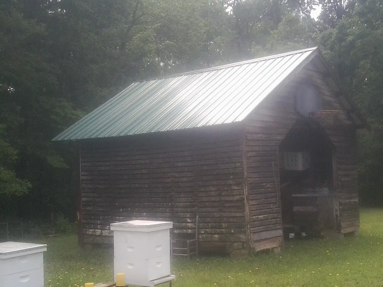 Green metal roof on a weathered barn beside stacked beehives in Amenia