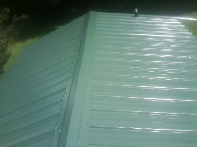 New green metal panels meeting at the ridge of a roof — Flat Roof Repair work by our crew in Amenia